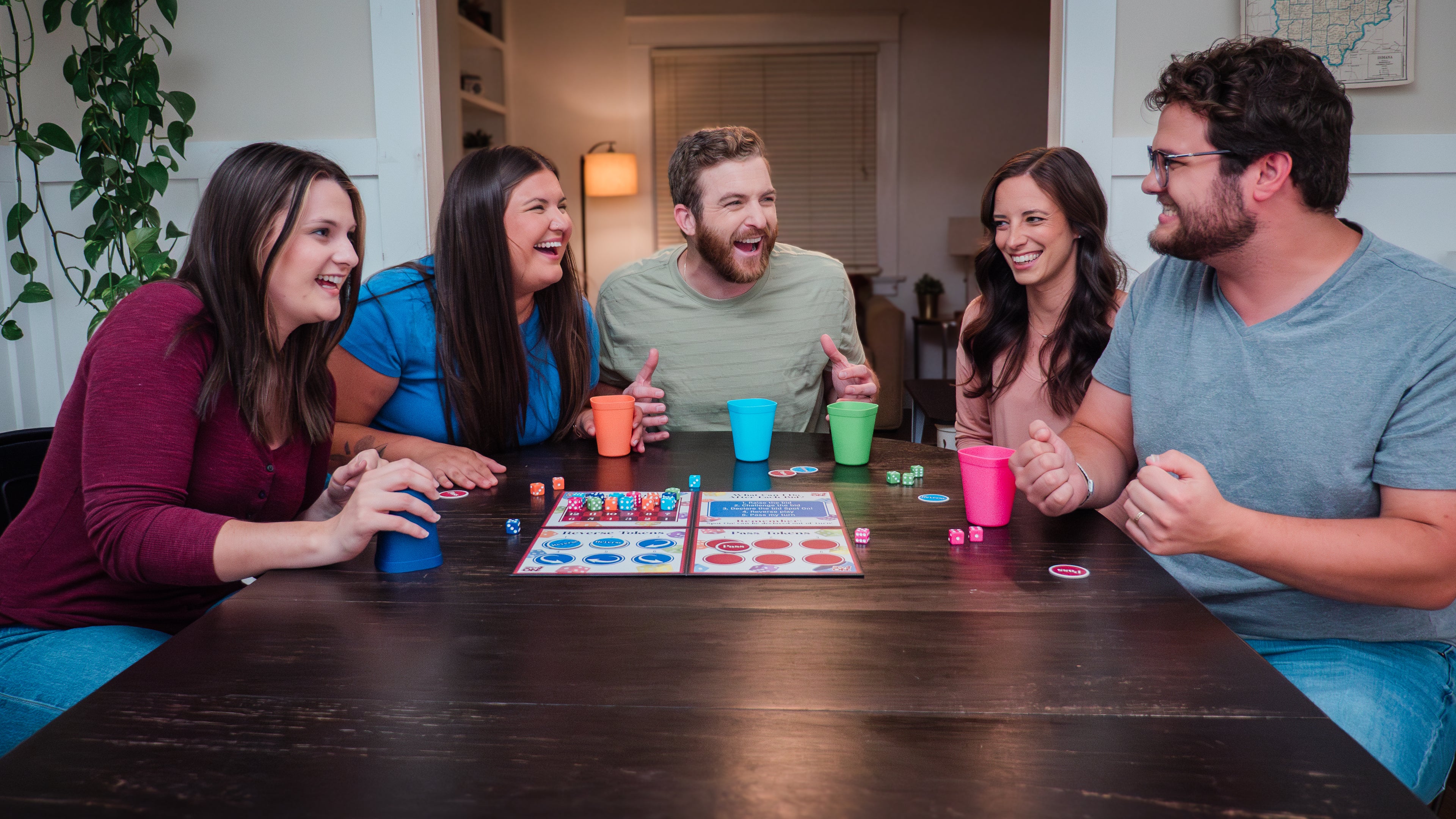 Load video: This is a video that demonstrates how to play That&#39;s Spot On! There are five players all having a super fun time bluffing, bidding, and challenging each other while shaking pretty dice in matching dice cups. The game board is also shown as well as the pass and reverse tokens.